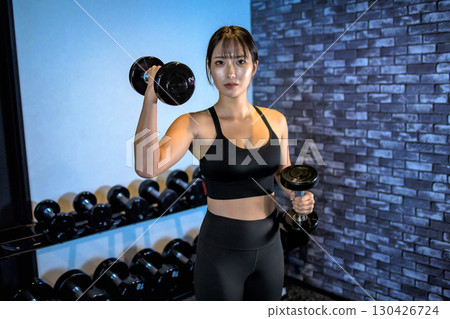 A woman lifting a dumbbell with one hand. A cool woman exercising at the gym. Upper body. Muscle training girl. 130426724