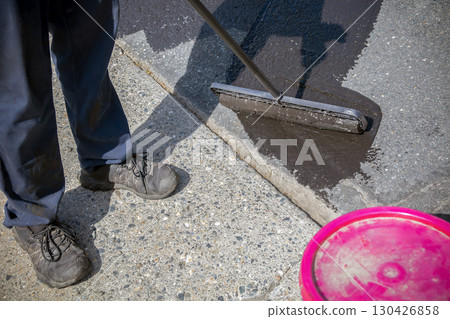 Worker applying asphalt protective coating with roller on driveway surface Worker applying asphalt protective coating with roller on driveway surface 130426858