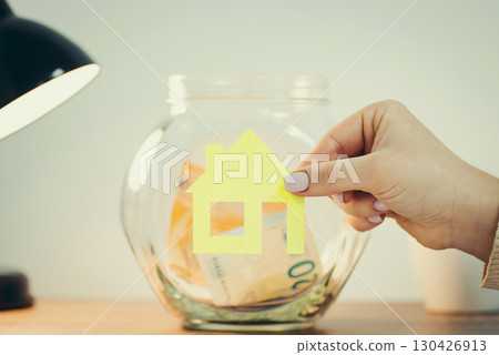 Putting house symbol on glass savings jar on the table, toned. Saving money for a new house, flat, place for living 130426913