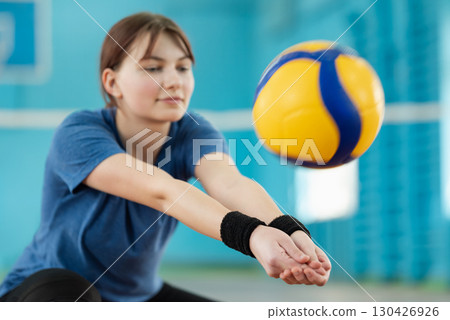 Practicing digging skills during volleyball training on court. Young girl practicing fundamental volleyball skills, physical education concept Practicing digging skills during volleyball training on court. Young girl practicing fundamental volleyball skills, physical education concept 130426926