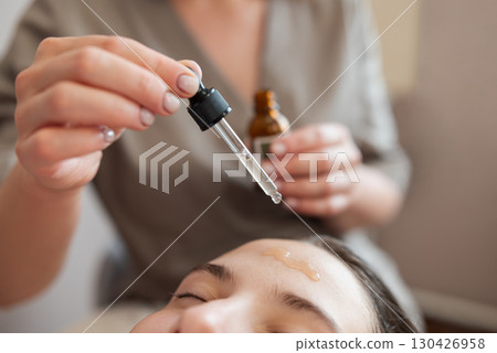 Microneedle mesotherapy in cosmetology clinic. Doctor drops some medicine to the forehead of a girl client before using meso roller with microneedles 130426958