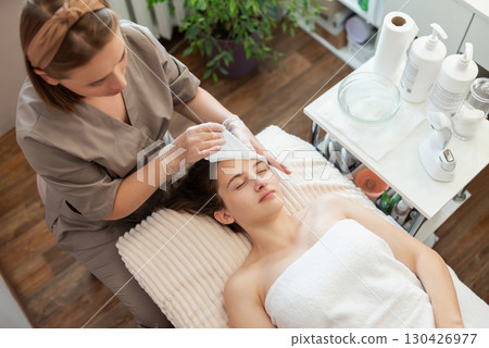 Washing and drying face of a female client before cosmetology procedures. Professional cosmetologist executing cleaning of a face in modern health and beauty clinic 130426977