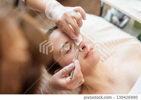 Skin care and cleaning in cosmetology clinic. Doctor cleaning pores on the client nose and face, using special cosmetology tools 130426990