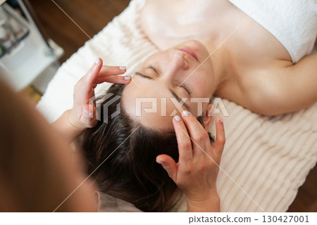 Back view of a doctor performing facial massage for reducing wrinkles, activating blood circulation, rejuvenation of skin. Treating facial skin by massage in cosmetological clinic Back view of a doctor performing facial massage for reducing wrinkles, activating blood circulation, rejuvenation of skin. Treating facial skin by massage in cosmetological clinic 130427001