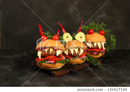 Halloween food ideas. Horrible hamburgers with fresh lettuce, tomatoes, cream cheese, lettuce, onion, cutlets and peppers in the shape of horns on an old concrete background. Halloween food concept, 130427194