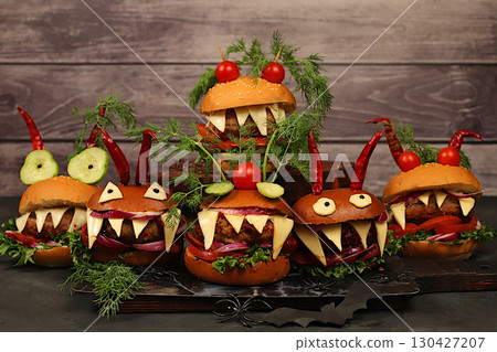 Horrible hamburgers with fresh lettuce, tomatoes, cream cheese, salad, onion, cutlets and peppers in the shape of horns on an old concrete background. Halloween food concept, cafe advertising Horrible hamburgers with fresh lettuce, tomatoes, cream cheese, salad, onion, cutlets and peppers in the shape of horns on an old concrete background. Halloween food concept, cafe advertising 130427207