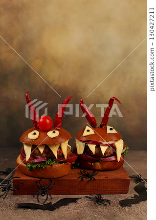 Horrible hamburgers with fresh lettuce, tomatoes, cream cheese, salad, onion, cutlets and peppers in the shape of horns on an old concrete background. Halloween food concept, cafe advertising, menu 130427211