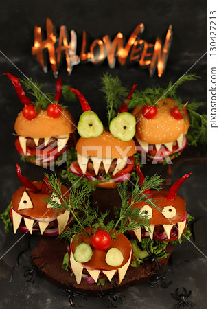 Horrible hamburgers with fresh lettuce, tomatoes, cream cheese, salad, onion, cutlets and peppers in the shape of horns on an old concrete background. Halloween food concept, cafe advertising, menu, 130427213