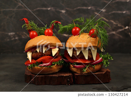 Horrible hamburgers with fresh lettuce, tomatoes, cream cheese, salad, onion, cutlets and peppers in the shape of horns on an old concrete background. Halloween food concept, cafe advertising, menu,. 130427214