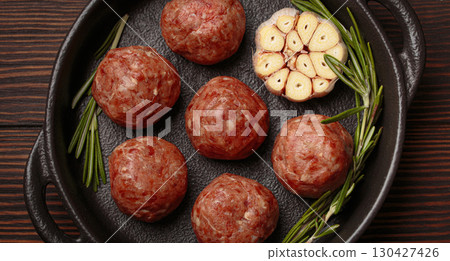Raw meatballs with garlic and rosemary in cast iron pan on wooden background 130427426