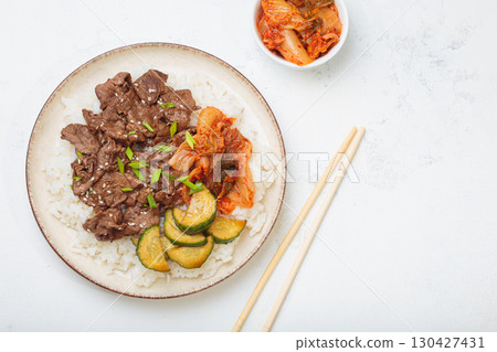 Korean beef bulgogi bowl dish with rice, roasted meat, kimchi and marinated cucumber on white background top view with chopsticks, space for text Korean beef bulgogi bowl dish with rice, roasted meat, kimchi and marinated cucumber on white background top view with chopsticks, space for text 130427431