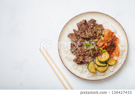 Korean beef bulgogi bowl dish with rice, roasted meat, kimchi and marinated cucumber on white background top view with chopsticks, space for text 130427433