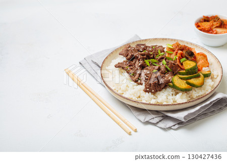 Korean beef bulgogi bowl dish with rice, roasted meat, kimchi and marinated cucumber on white background with chopsticks, space for text 130427436