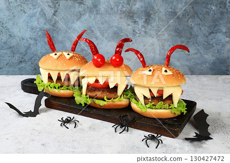Halloween food concept. Scary hamburgers with fresh parsley leaves, tomatoes, cream cheese, lettuce, onion and cutlet on an old concrete background, food delivery, 130427472