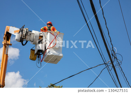 Electrical lineman in bucket truck working on power lines against blue sky 130427531