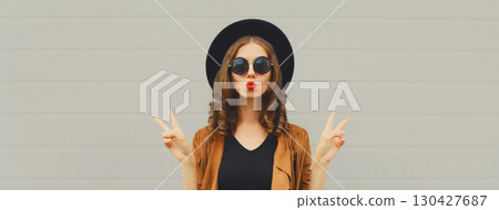 Portrait of beautiful young woman blowing kiss, stylish girl in black hat posing on gray background Portrait of beautiful young woman blowing kiss, stylish girl in black hat posing on gray background 130427687