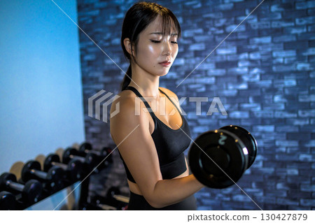 Woman lifting dumbbells, cool woman exercising at the gym, dumbbell curl, muscle training girl 130427879
