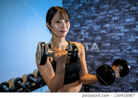 一位女士正在用啞鈴訓練手臂。一位酷炫的女士正在健身房鍛鍊。啞鈴彎舉。肌肉訓練女孩。 130428067