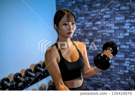 一位女士正在用啞鈴訓練手臂。一位酷炫的女士正在健身房鍛鍊。啞鈴彎舉。肌肉訓練女孩。 130428070