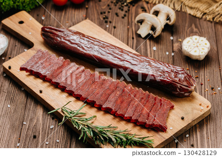 Sliced cured sausage with whole piece on wooden board and spices, rustic food styling 130428129