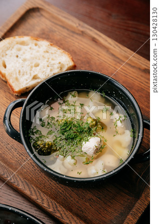 Clear soup with vegetables and chicken meatballs, served with rustic bread on wooden tray 130428130
