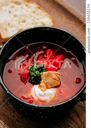 Traditional Ukrainian borscht with sour cream, pork, and fresh herbs in a black rustic bowl Traditional Ukrainian borscht with sour cream, pork, and fresh herbs in a black rustic bowl 130428134
