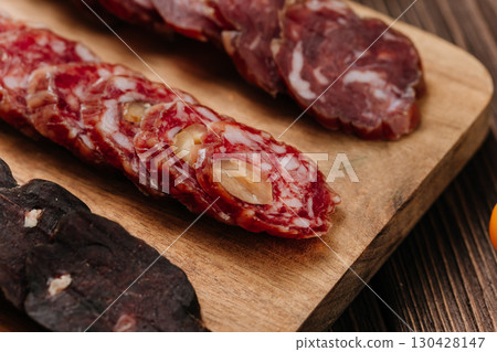 Close-up of gourmet sliced sausage with nuts on wooden board, traditional cured meat snack 130428147