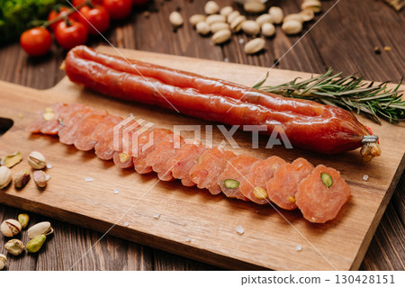 Sliced gourmet sausage with pistachios on wooden board with herbs and vegetables 130428151