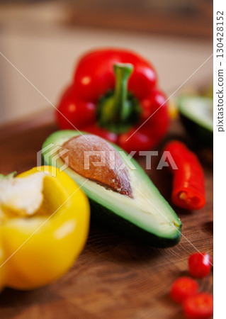 Close-up of fresh avocado with seed, bell pepper and chili on rustic wooden kitchen table 130428152