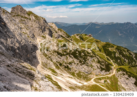 Hiking Trail From Alpspitze Via Ferrata In The Bavarian Alps: Scenic Mountain Path With Rocky Slopes And Green Valleys Under Clear Blue Sky 130428409