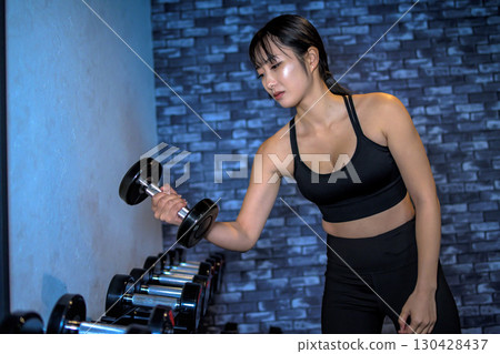 A woman choosing the weight of a dumbbell. A cool woman exercising at the gym. A woman doing muscle training. 130428437