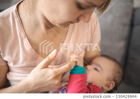 Mother breastfeeding her baby in a cozy indoor setting during daytime 130428664