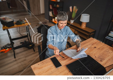 Architect reviewing blueprints in her home office during renovation works 130428705
