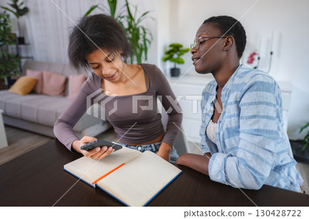 Two young women studying together at home using smartphone and notebook Two young women studying together at home using smartphone and notebook 130428722