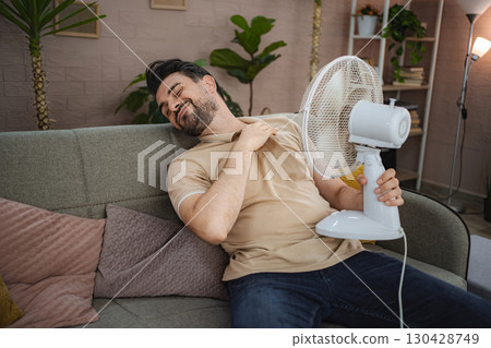 Man refreshing himself with a fan during a heat wave at home 130428749