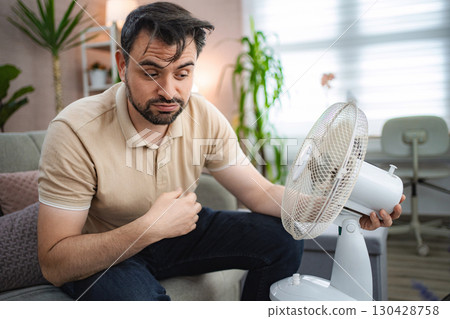 Man refreshing himself with a fan during a heat wave at home Man refreshing himself with a fan during a heat wave at home 130428758