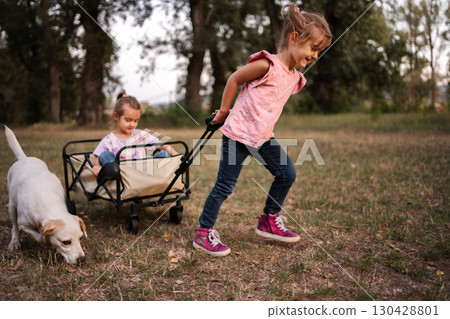Two little sisters pulling a wagon with their dog in a park Two little sisters pulling a wagon with their dog in a park 130428801