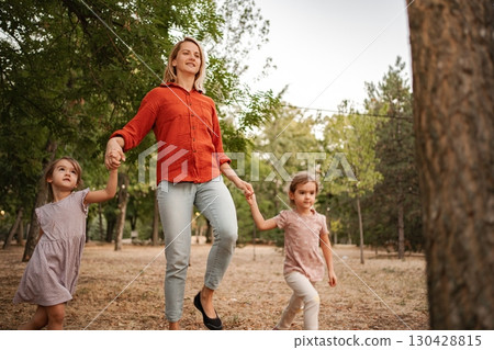 Mother walking in the park holding hands with her two daughters 130428815
