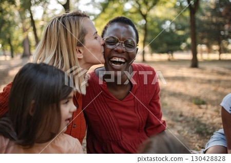 Woman kissing her friend on the cheek while sitting in a park 130428828