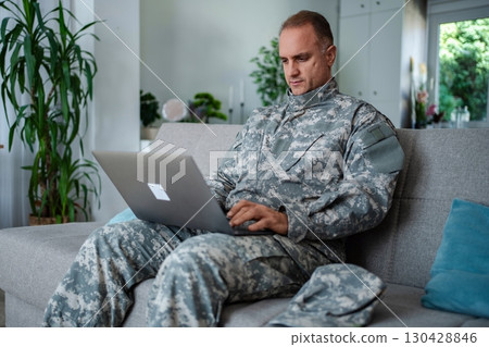 Soldier in camouflage uniform using laptop on sofa at home Soldier in camouflage uniform using laptop on sofa at home 130428846