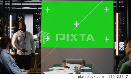 Black male supervisor hosting a late meeting with chroma key display in the boardroom of a multinational company at night, reviewing proposals and making decisions for business future. Camera A. Black male supervisor hosting a late meeting with chroma key display in the boardroom of a multinational company at night, reviewing proposals and making decisions for business future. Camera A. 130428847