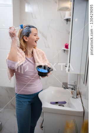 Woman dyeing her hair blue in the bathroom, smiling and looking in the mirror 130429095