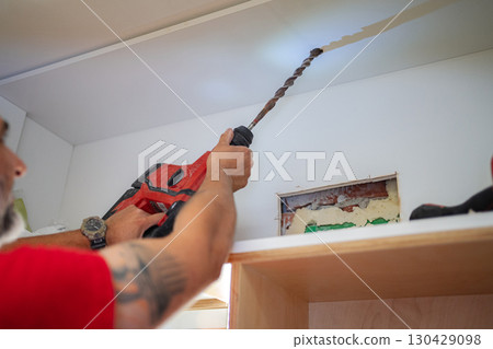 Contractor drilling a hole in the ceiling using a hammer drill 130429098