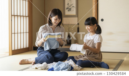 Daughter helping mother fold laundry Daughter helping mother fold laundry 130429584