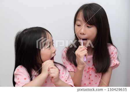 Two sisters, ages 4 and 10, brushing their teeth in pajamas 130429635