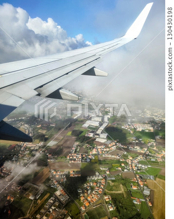 Airplane wing above lush green fields and urban areas, capturing the beauty of nature and cityscape during flight, showcasing the journey from above with stunning cloud formations Airplane wing above lush green fields and urban areas, capturing the beauty of nature and cityscape during flight, showcasing the journey from above with stunning cloud formations 130430198