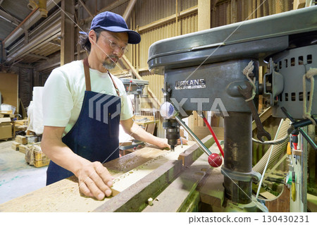 Woodworker drilling holes in wood with a drill press 130430231