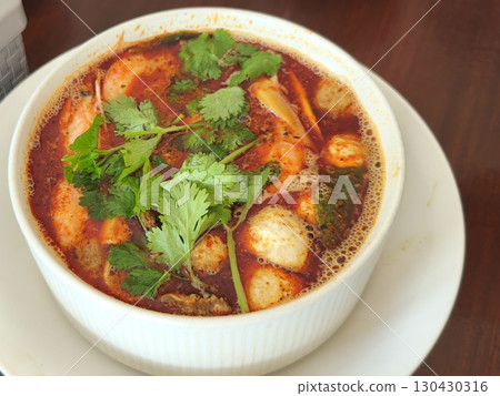 Hot and steamy bowl of tom yum soup with shrimp, mushrooms, and herbs in a spicy red broth, served fresh in a white ceramic bowl. 130430316