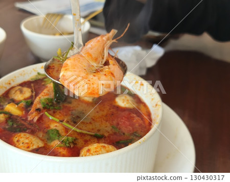 Hot and steamy bowl of tom yum soup with shrimp, mushrooms, and herbs in a spicy red broth, served fresh in a white ceramic bowl. 130430317