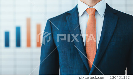professional in blue suit and orange tie stands confidently in front of blurred bar graph, symbolizing business growth and success 130431352